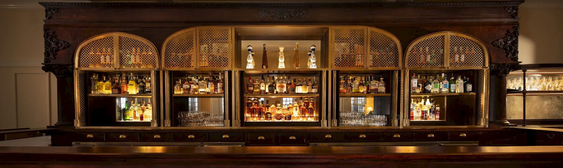 A classic bar setup with a wooden counter, shelves of various liquor bottles, and glasses neatly arranged for service.