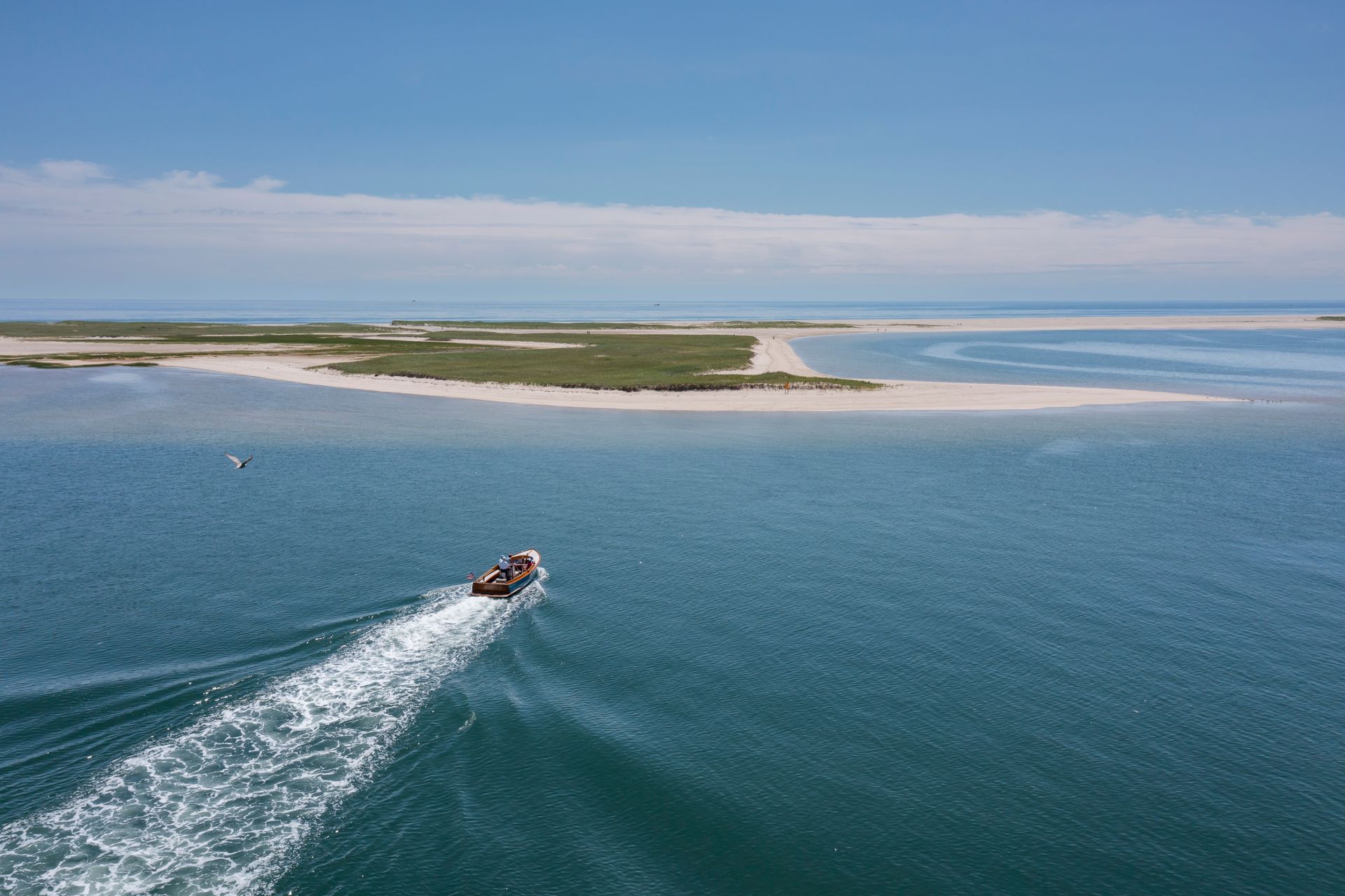 A small boat travels on blue waters near an island with sandy beaches and grassy patches under a clear blue sky.