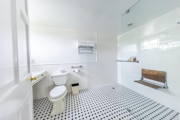 A clean, white bathroom with a glass shower, wooden seat, toilet, and towel rack on a tile floor.