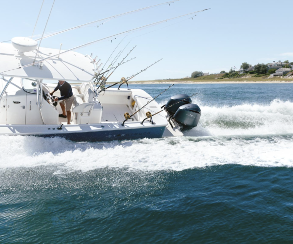 A motorboat with fishing rods cutting through the water, creating a wake, with a coastal backdrop.
