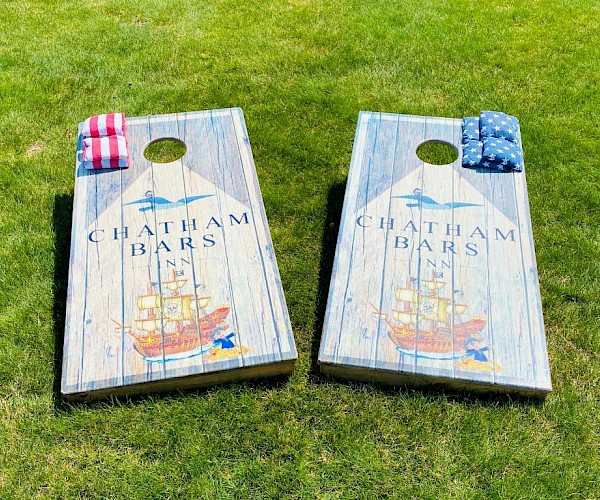Two cornhole boards with a ship design and "Chatham Bars Inn" text on grass, featuring red and blue bean bags.
