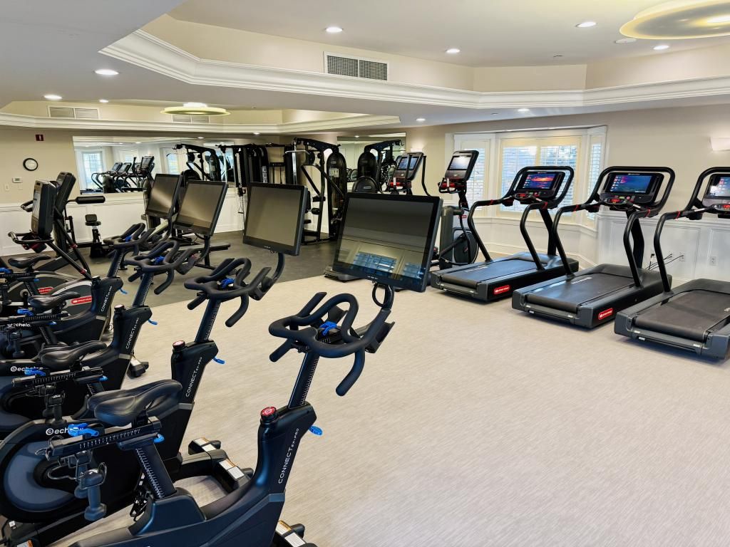 The image shows a modern gym with exercise bikes and treadmills, each equipped with digital screens.